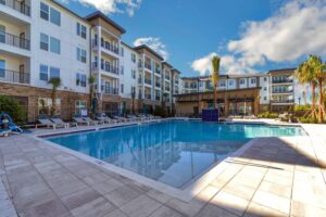 Modern apartment complex with large outdoor pool and lounge chairs on a sunny day.