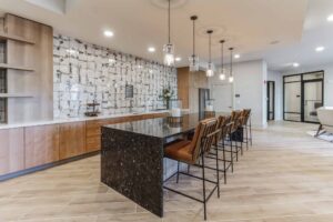 Modern kitchen interior with large island, sleek chairs, pendant lighting, and wood cabinetry.