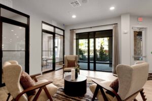 Modern lounge with beige armchairs, round table, glass doors, and terrace view. Cozy and stylish interior design.