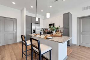 Modern kitchen with granite island, stylish lighting, and sleek grey cabinetry. Cozy seating for two at the counter.