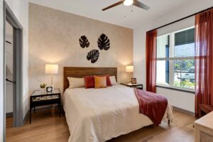 Warm and cozy bedroom with wall art, large bed, and natural light from a window with red curtains.
