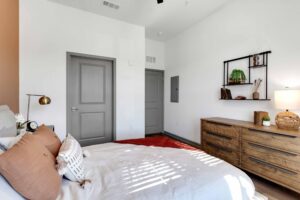 Minimalist bedroom with wooden dresser, cozy bed, wall shelves, and stylish decor accents.