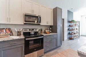 Modern kitchen with gray cabinets, granite countertops, stainless steel appliances, and wall shelf decor.
