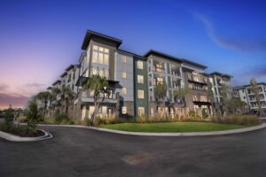 Modern apartment building with balconies, surrounded by palm trees at sunset.