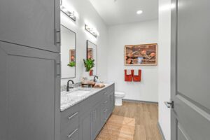 Modern bathroom with gray cabinets, double sinks, framed art, and wood flooring.