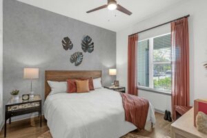 Modern bedroom with gray accent wall, wood bedframe, and red curtains. Cozy ambiance with artistic leaf decor.
