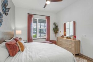 Modern bedroom with cozy bed, decorative pillows, dresser, and large window with red curtains.