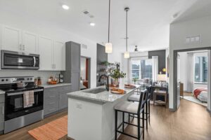 Modern kitchen and living area with sleek design, bar seating, and natural light from large windows.