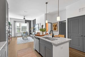 Modern open-concept living room with kitchen island, stylish decor, and natural light from large windows.