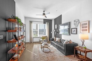 Modern living room with black leather sofa, wooden shelves, and large window for natural light.