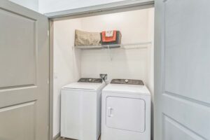 Compact laundry closet with washer, dryer, and shelf for organizing essentials.