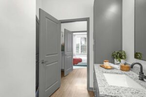 Modern bathroom with granite countertop, view of bedroom through open doors. Bright and minimalistic home interior.