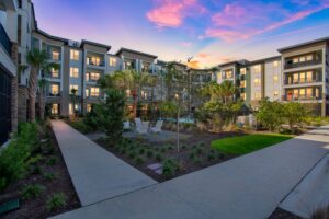 Modern apartment complex with landscaped courtyard and outdoor seating at sunset.